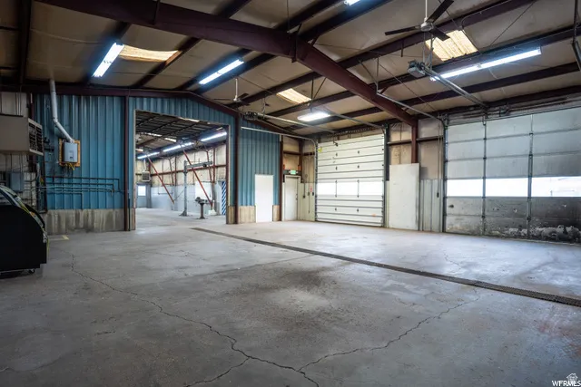 Concrete flooring, exposed structural beams, fluorescent lighting, two large roll-up doors, and corrugated metal wall panels