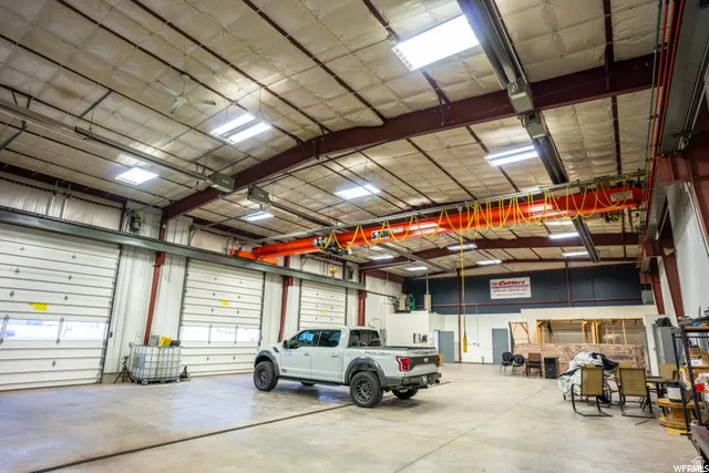 Warehouse space featuring multiple overhead garage doors, high ceilings, exposed metal beams, skylights, and fluorescent lighting