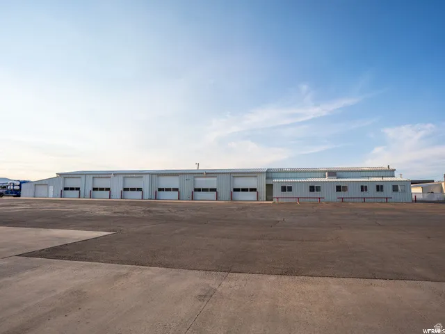 Expansive asphalt and concrete lot with a large metal-clad building featuring multiple roll-up doors and several windows