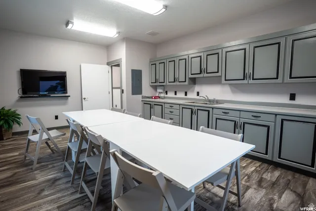 Extensive cabinetry with dark hardware and paneling, a stainless steel sink, and wood-finish flooring