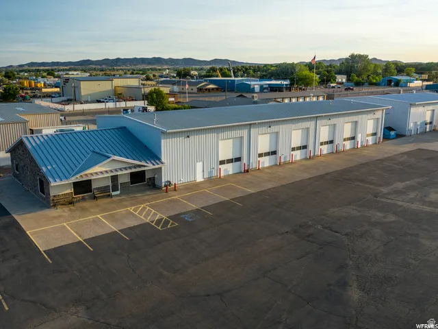 Commercial building featuring a stone and siding exterior, a metal roof, multiple roll-up doors, and an expansive paved lot with marked parking spaces