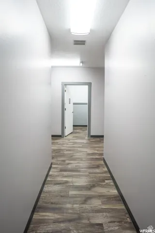 Hallway with wood-finish flooring, white walls, and overhead fluorescent lighting