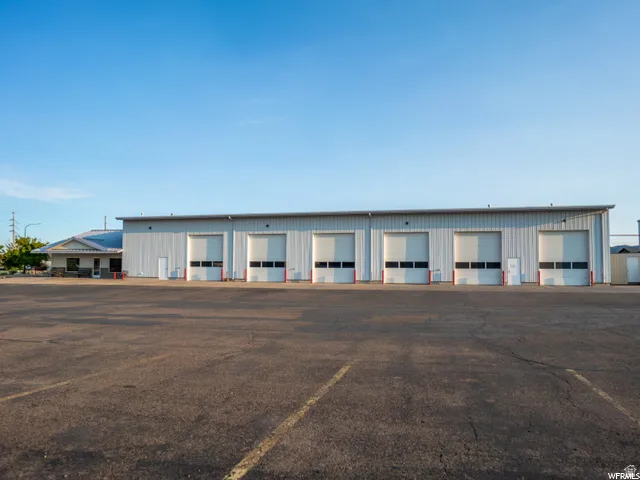 Industrial building featuring multiple bay doors, an attached office space, a large paved lot, and a metal roof
