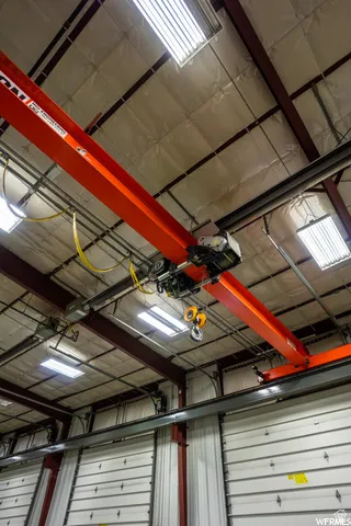 Industrial ceiling with exposed structural beams, overhead gantry crane system, multiple fluorescent light fixtures, and insulated ceiling panels