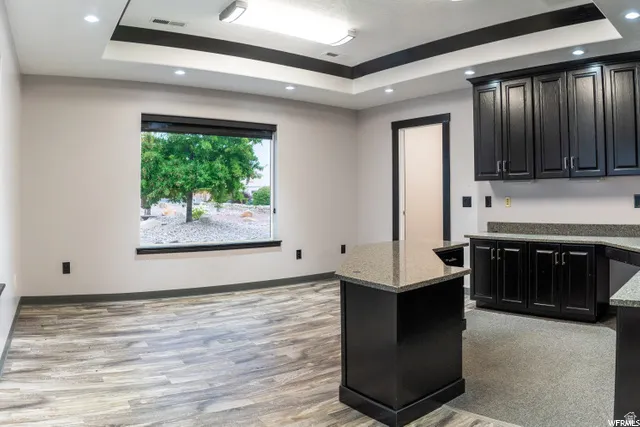 Recessed lighting, tray ceiling, wood-finish flooring, dark cabinetry, and light-toned countertops