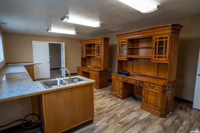 Wood-finish flooring, two large built-in desks with upper cabinetry, a stainless steel double basin sink, and ceiling-mounted linear lighting fixtures