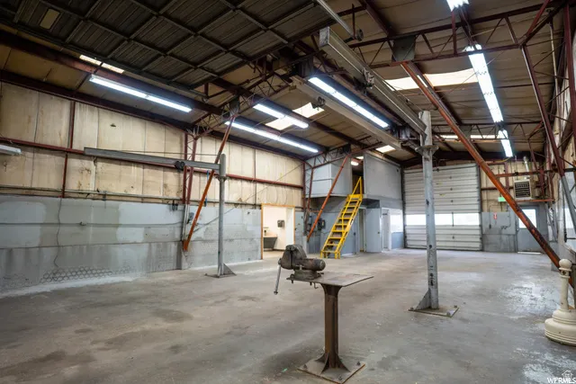 Large open industrial space featuring multiple overhead doors, exposed structural beams, fluorescent lighting, and a durable concrete floor