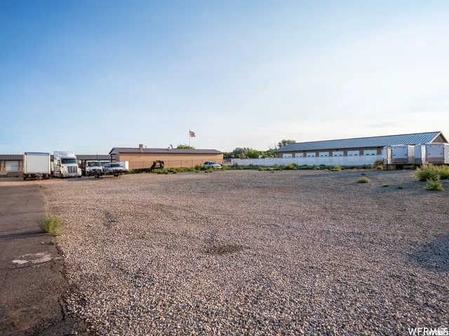 Gravel lot with surrounding buildings featuring roll-up doors and a metal roof structure