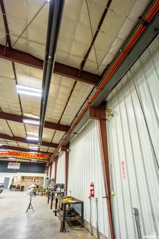 Insulated ceiling with exposed structural beams, corrugated metal wall panels, and concrete flooring