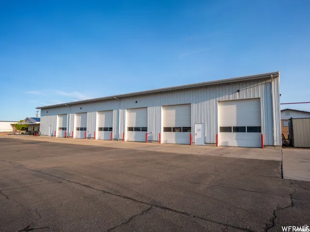 Metal-sided commercial building featuring multiple roll-up doors, an asphalt parking area, and a flat roofline