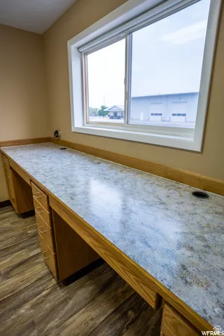 Built-in desk with wood-finish cabinetry, patterned countertop, and wood-finish flooring