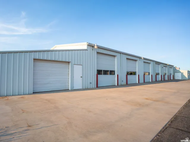 Metal-clad industrial building featuring multiple overhead doors, individual pedestrian entrances, and an expansive concrete lot