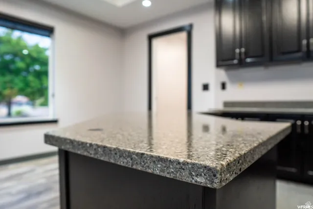 Kitchen island with a speckled countertop, dark cabinetry, and wood-finish flooring