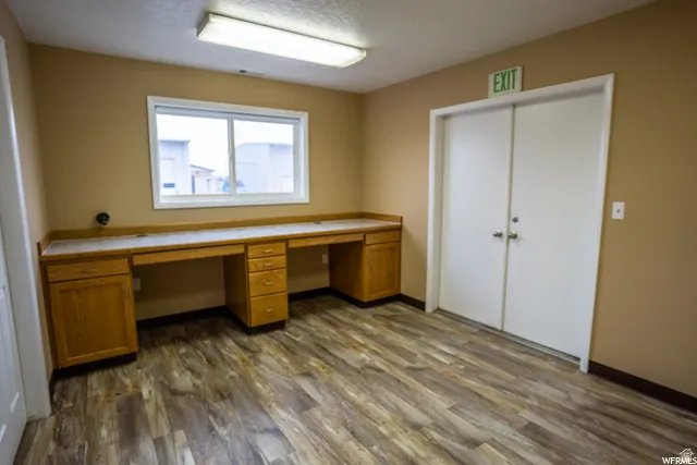 Wood-finish flooring, built-in wooden desk, dual entry doors, window, and overhead lighting