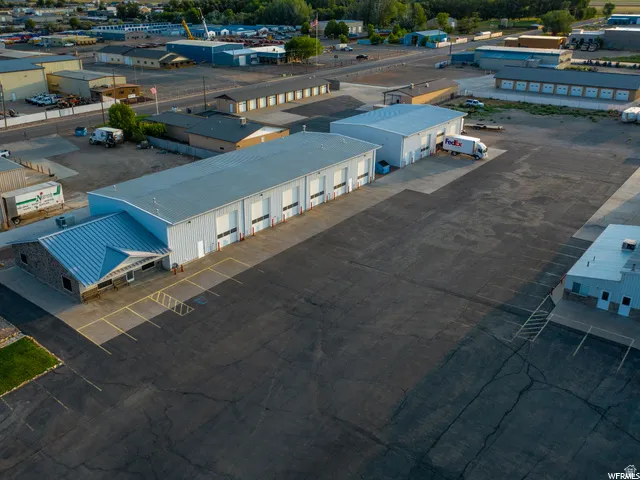 Expansive paved lot with multiple industrial buildings, featuring a stone-clad office entrance, several overhead doors, and ample parking