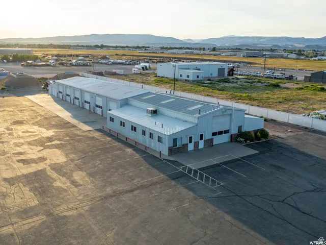 Industrial building with multiple bay doors, metal siding, a flat roof, and an expansive paved lot