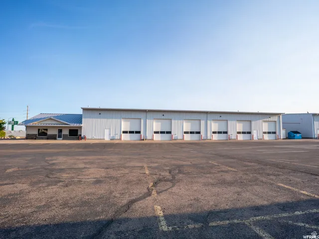 Asphalt parking area with multiple cracks, commercial building featuring a stone facade and metal roofing, and six roll-up garage doors