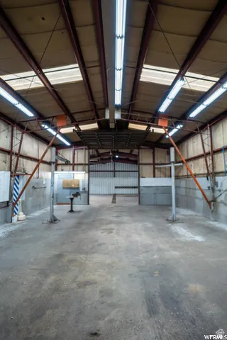 Spacious interior with exposed steel beam construction, multiple fluorescent light fixtures, and a concrete floor