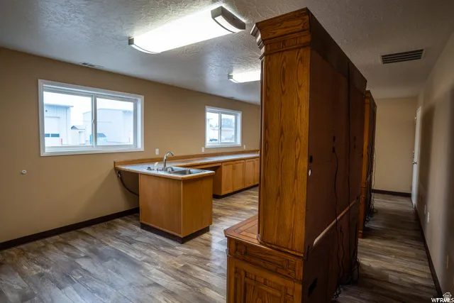 Expansive room featuring wood-finish flooring, two large sliding windows, extensive cabinetry with integrated sink, and overhead fluorescent lighting
