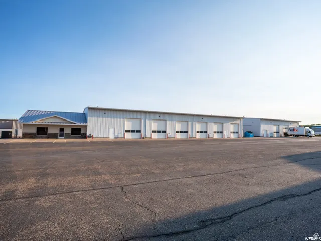 Commercial structure featuring a large asphalt parking area, multiple overhead bay doors, and a partial stone facade