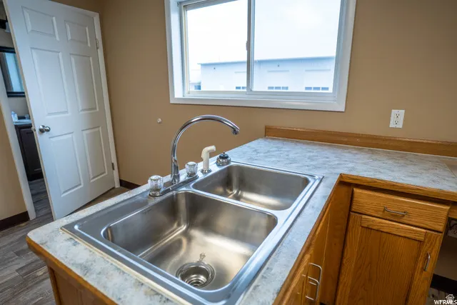 Dual basin stainless steel sink with chrome faucet, wood-finish cabinetry, and a countertop with integrated backsplash