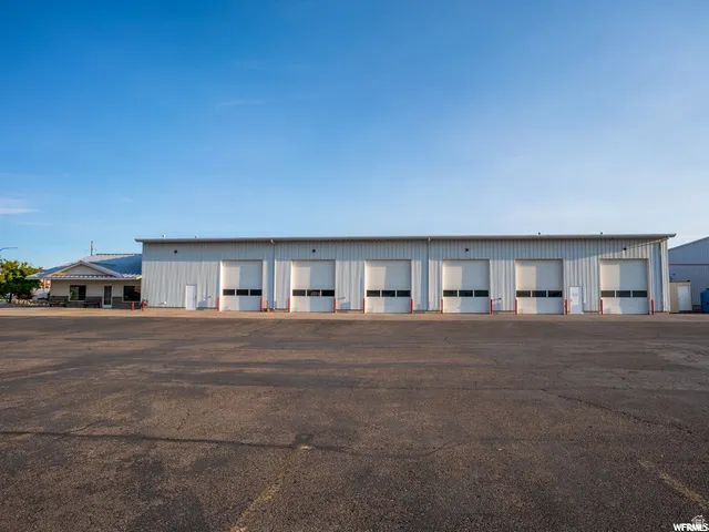 Metal-sided building with multiple roll-up doors, an asphalt parking area, and an attached office structure with a shingled roof