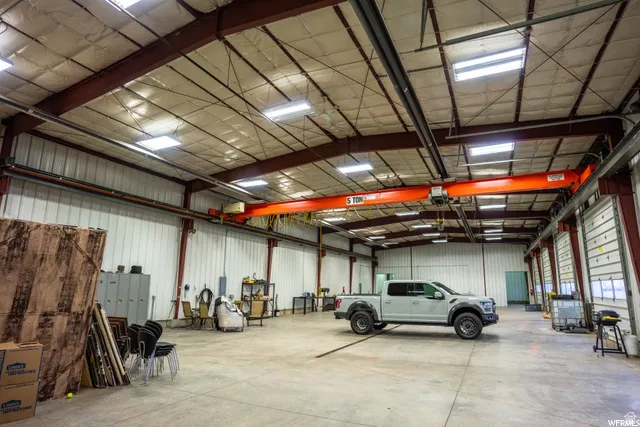 Spacious industrial interior featuring a concrete floor, exposed structural beams, ceiling-mounted lighting, and multiple roll-up doors