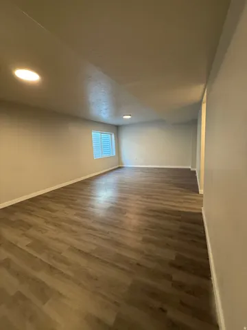 Spacious room featuring laminate wood-finish flooring, recessed lighting, and a window with white louvered blinds