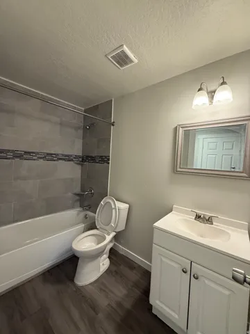 Bathroom featuring wood-finish flooring, a white vanity with an integrated sink, a framed mirror, and a tub with tiled surround
