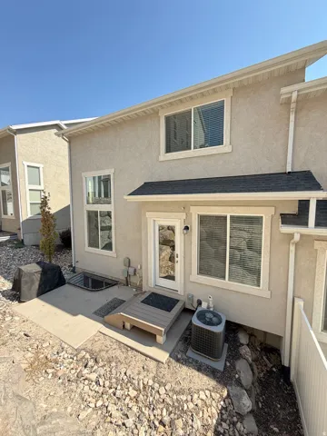 Stucco exterior with white trim, multiple windows with blinds, a back entrance with a small deck, and a window well