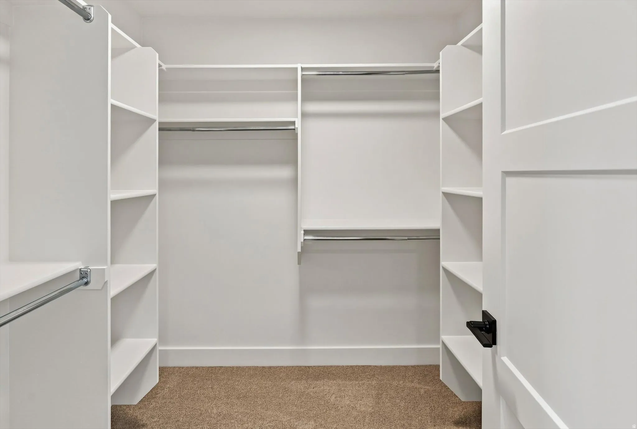 Walk-in closet with integrated shelving units, multiple chrome hanging rods, and neutral-toned carpeting