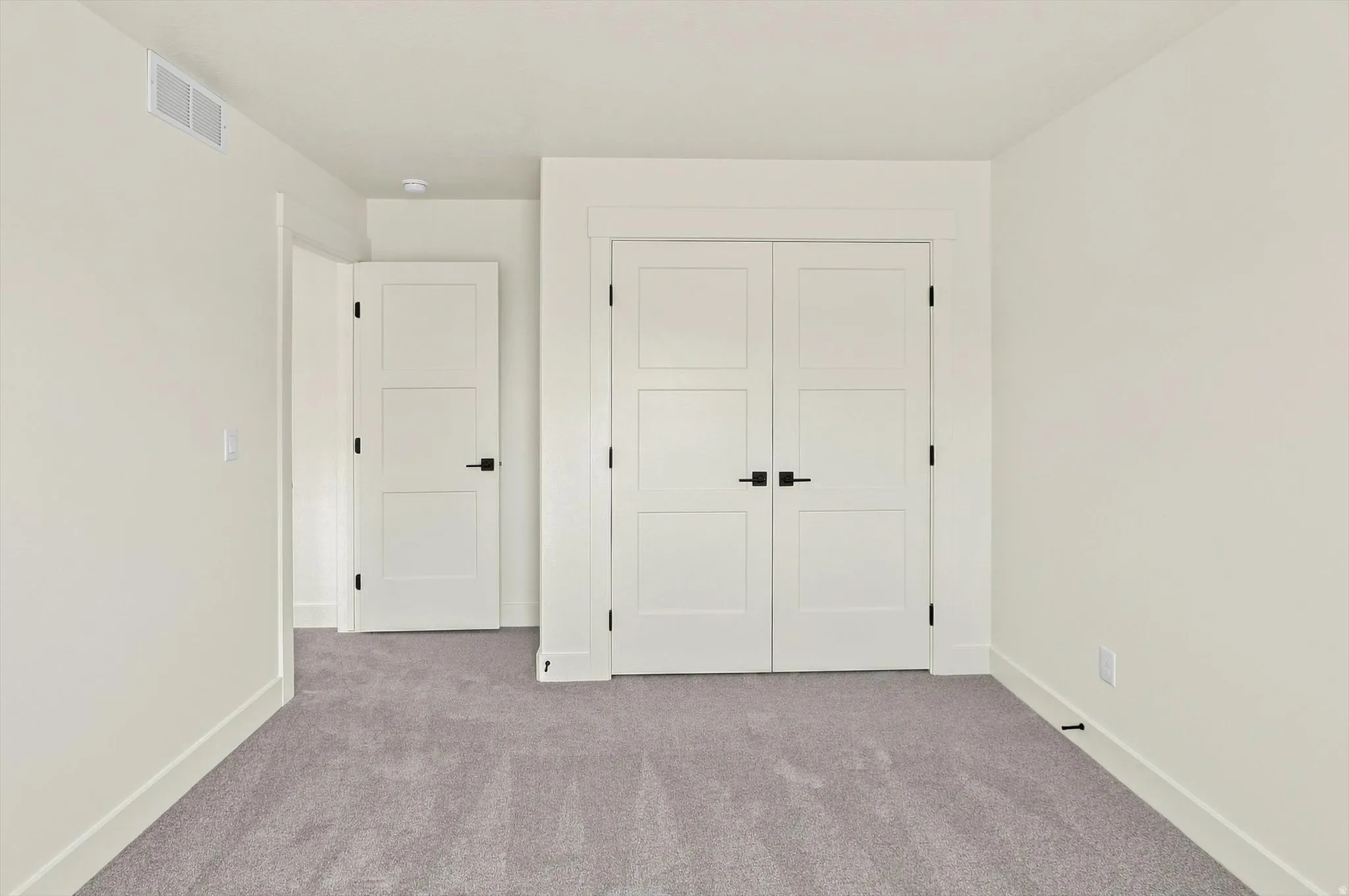 Neutral-toned carpeting, white walls, white trim, and white doors with matte black hardware