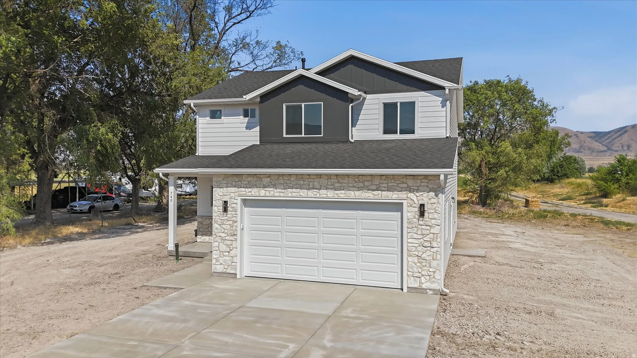 Two-story residence featuring light-colored siding, stone facade, and a two-car garage