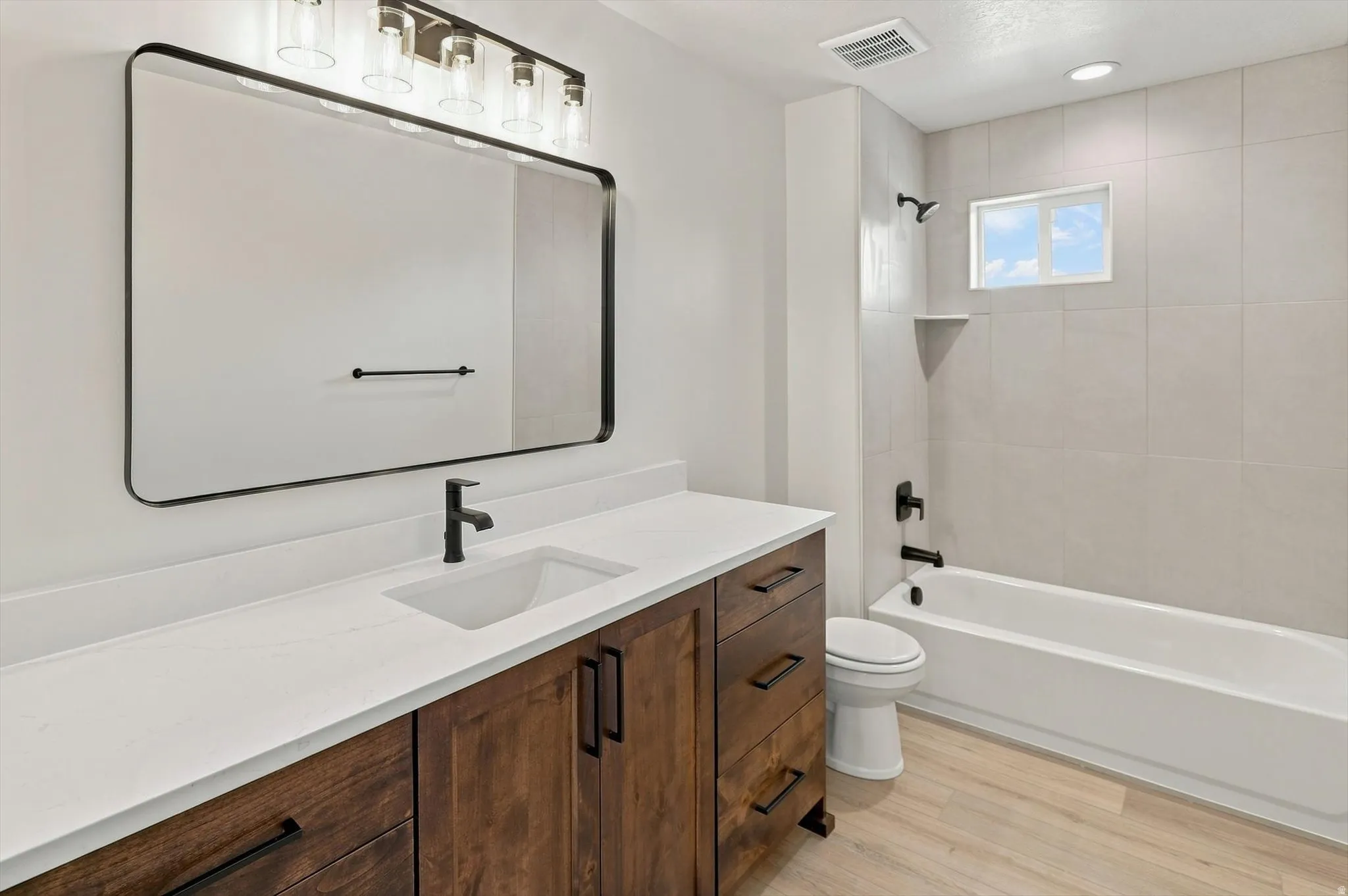 Modern bath featuring a wood-finish vanity, white countertop, and rectangular undermount sink