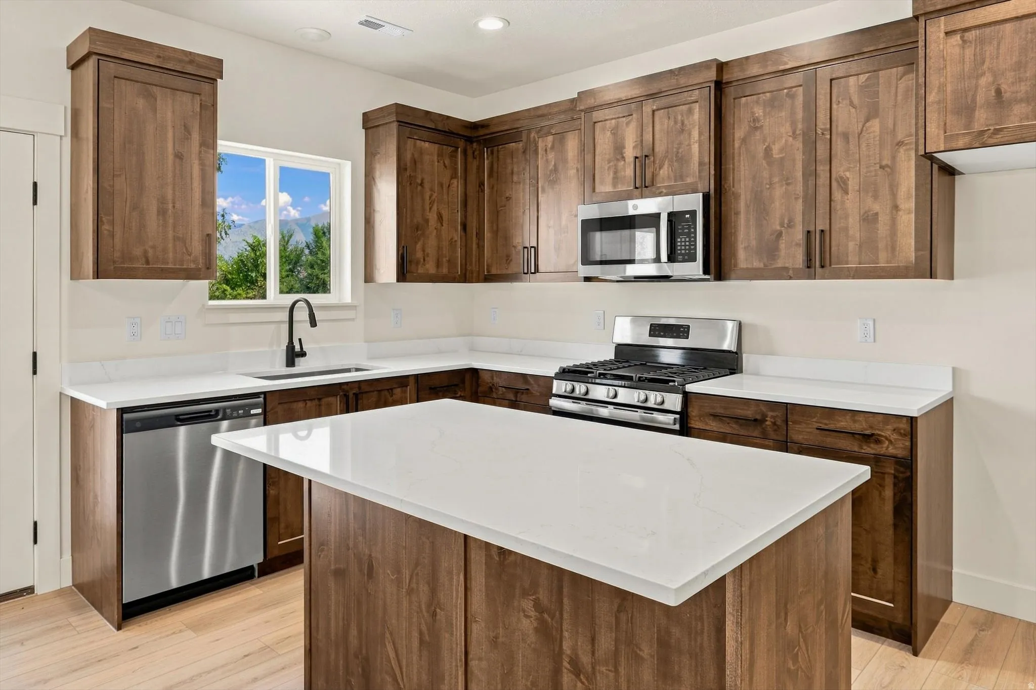 Kitchen featuring wood-finish cabinetry, white countertops, stainless steel appliances, and a central island