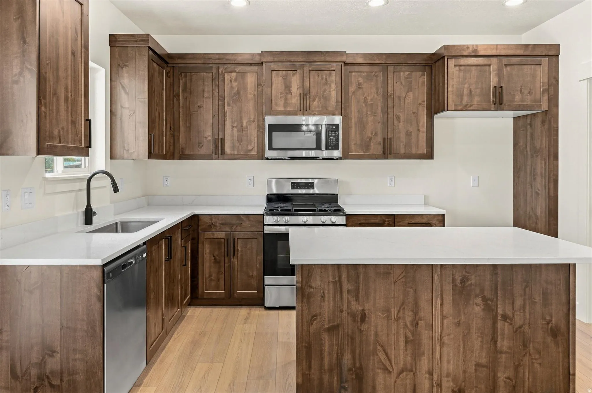 Kitchen featuring wood cabinetry, white countertops, stainless steel appliances, and wood-finish flooring
