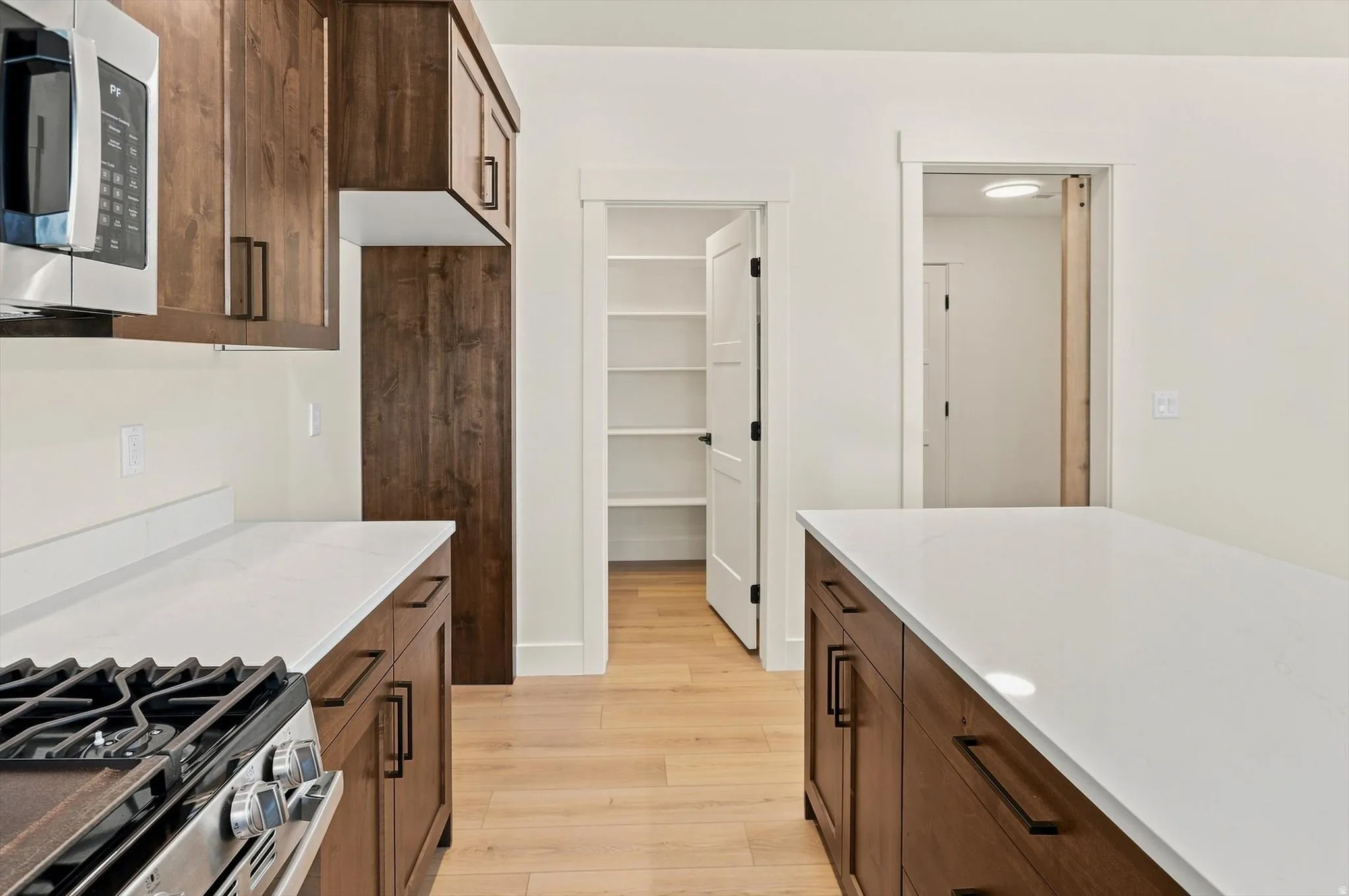 Wood-finish cabinetry with matte black hardware, stainless steel gas range, and white countertops