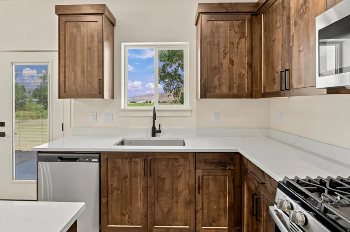 Kitchen featuring wood-finish cabinetry, light countertops, stainless steel appliances, and a window above the sink