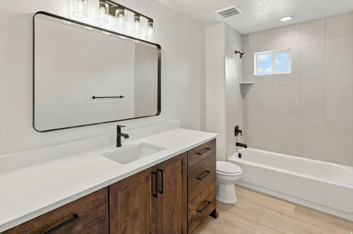 Modern bath featuring a wood-finish vanity, white countertop, and rectangular undermount sink