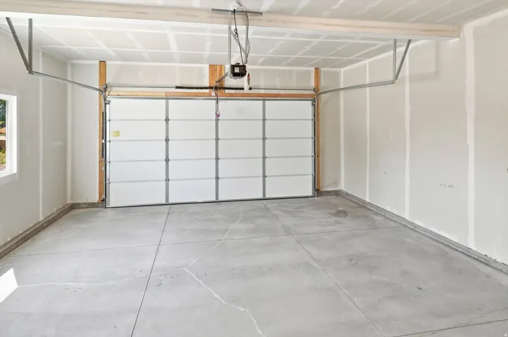 Attached garage featuring a white sectional door, concrete flooring, and a window