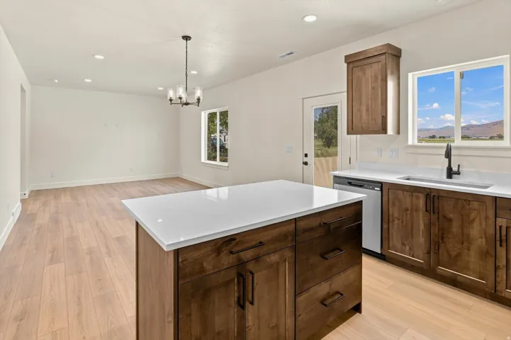 Kitchen featuring dark wood-finish cabinetry, white countertops, a stainless steel dishwasher, and a black faucet