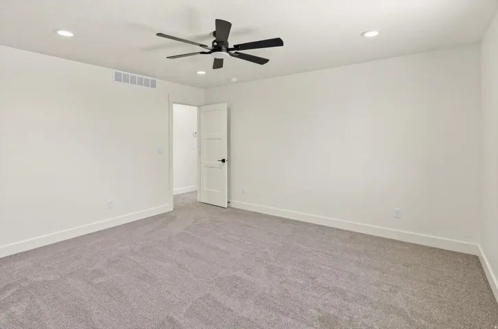Recessed lighting, ceiling fan with matte black finish, light gray carpeting, white painted walls, and a two-panel interior door