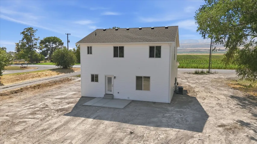 White siding exterior, multiple windows, rear entry door, and a ground-level concrete patio