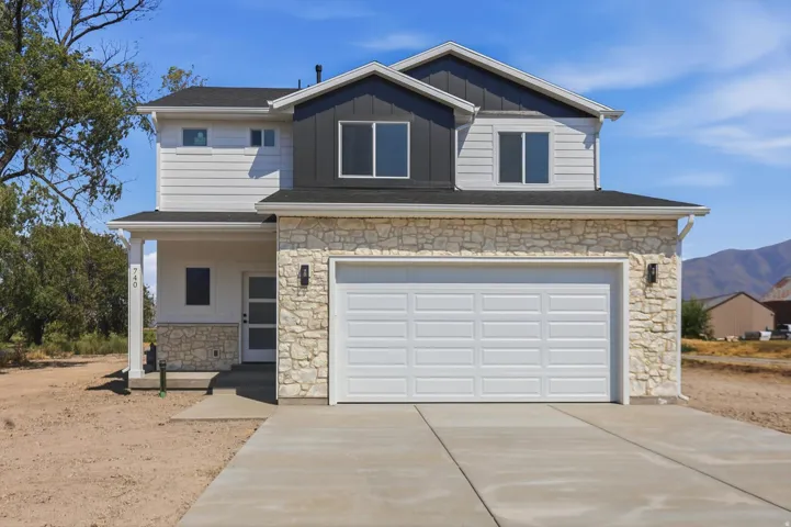 Two-story residence featuring light-toned stone veneer and siding, attached garage, covered entry, and a concrete driveway
