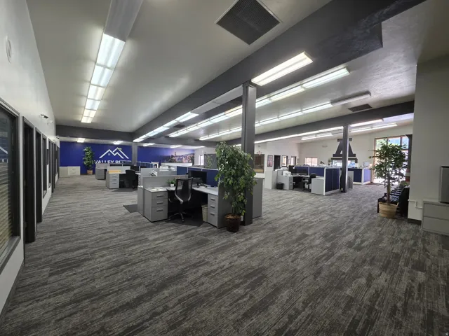 Open-plan office area featuring patterned carpet flooring and abundant overhead lighting