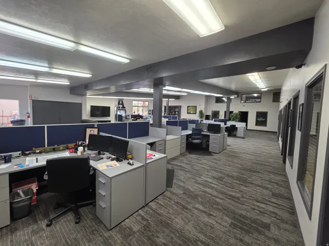 Spacious open-plan office featuring carpet flooring, built-in cubicle workstations, recessed lighting, and individual offices with glass-paneled doors