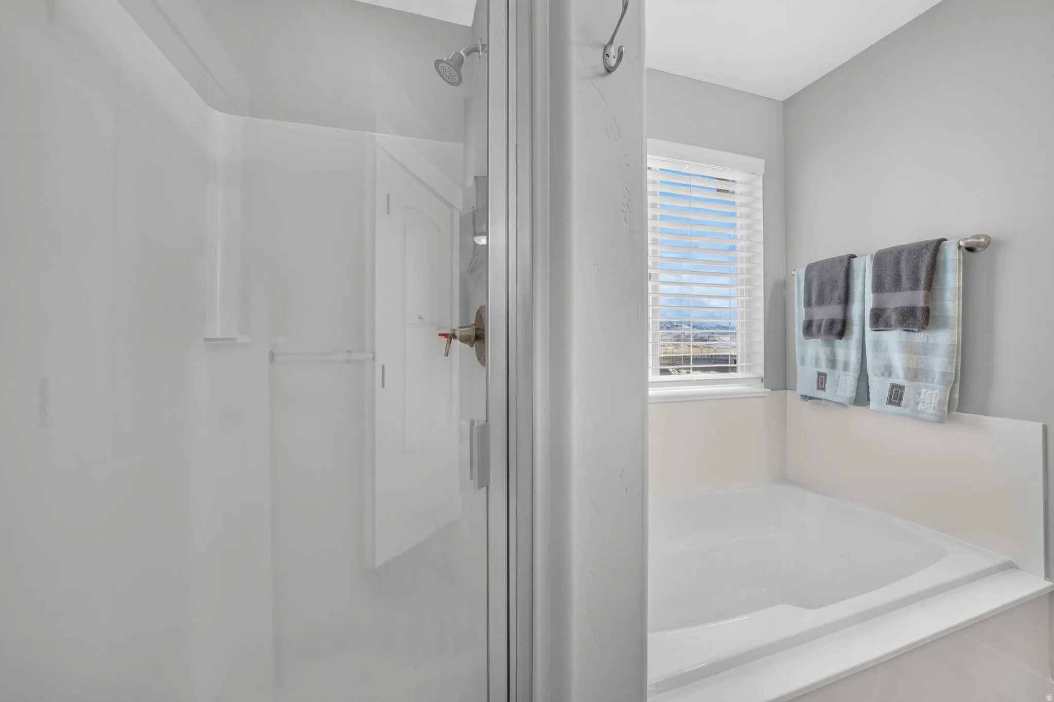 Glass-enclosed shower with brushed nickel fixtures, built-in soaking tub, and window with horizontal blinds