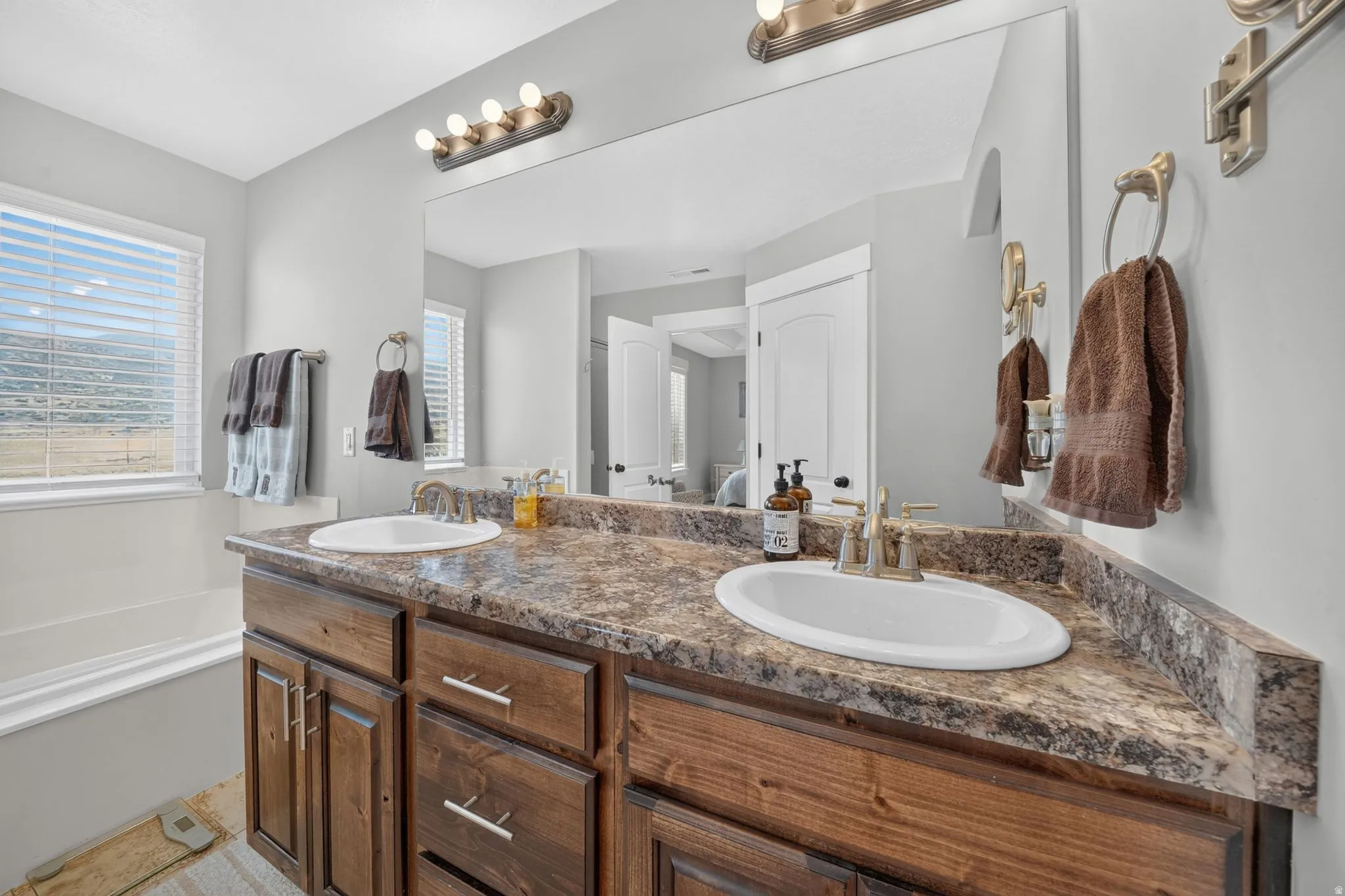 Dual vanity with wood-finish cabinetry, an expansive mirror, and a built-in soaking tub
