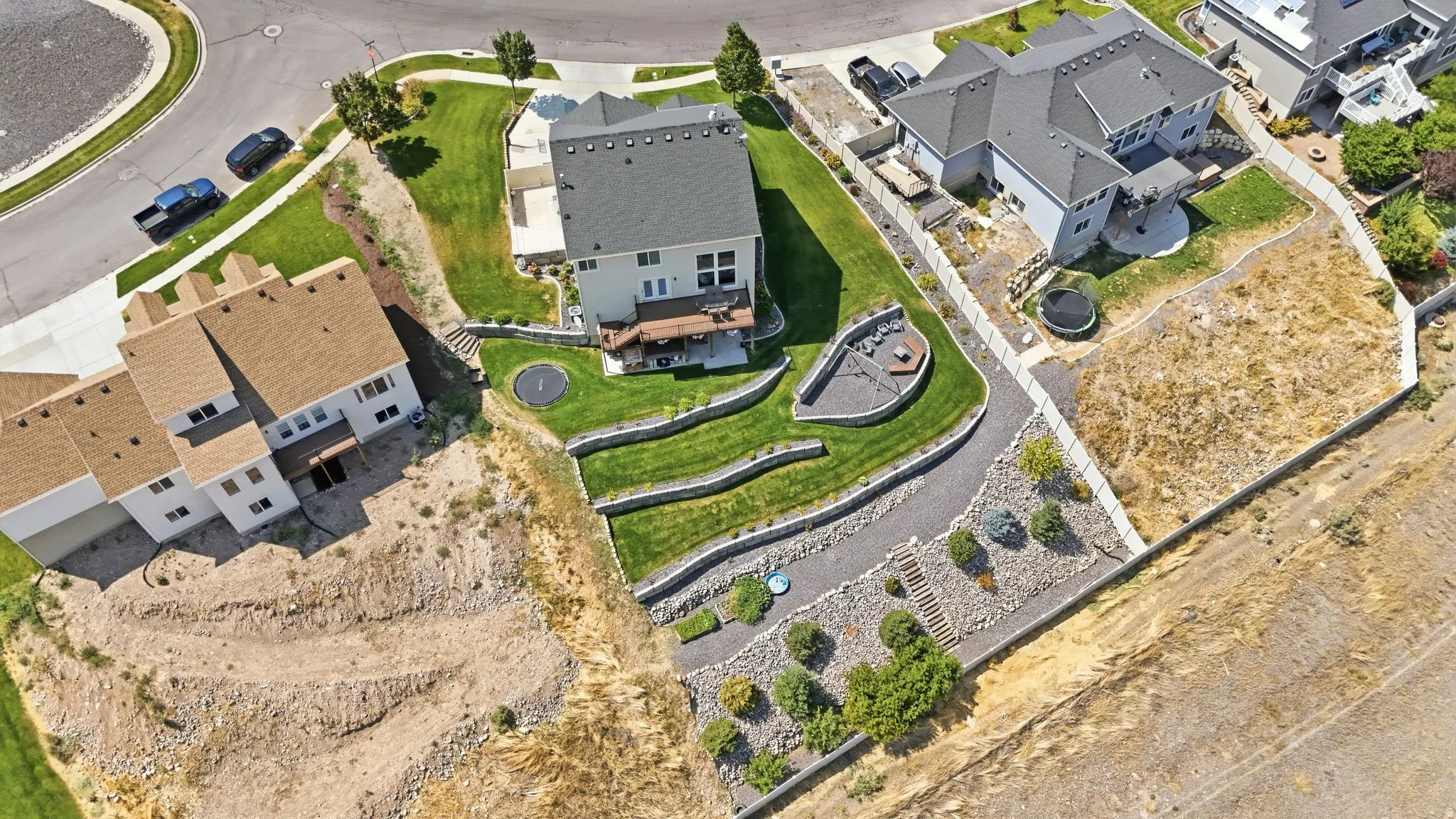 Terraced backyard with manicured lawn, established landscaping, and a built-in fire pit area