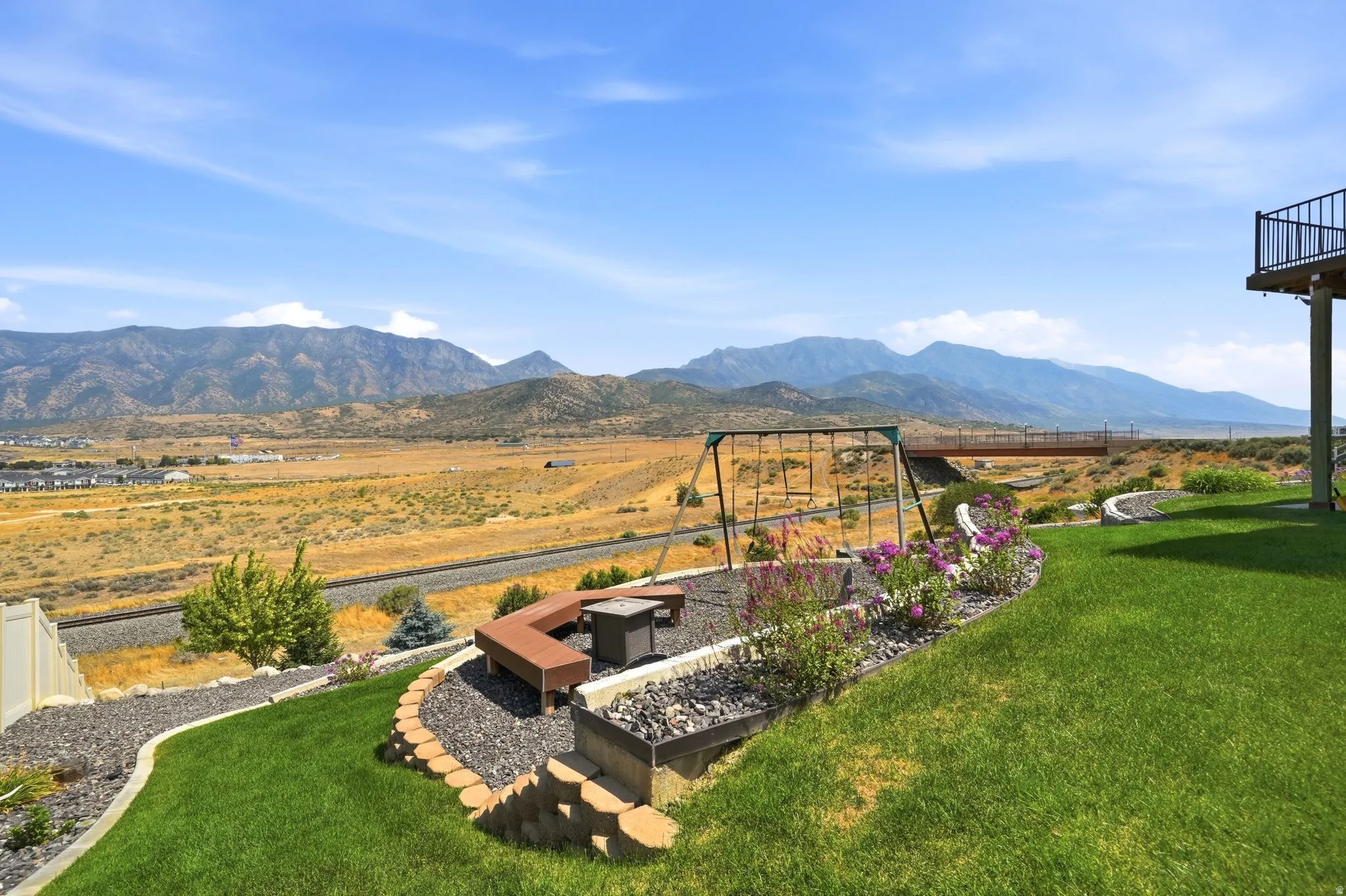 Expansive backyard featuring a manicured lawn, tiered landscaping with stone retaining walls, and a built-in fire pit with bench seating